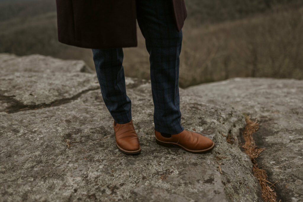 Close-up picture of a person’s brown dress shoes while standing on top of a large rock.