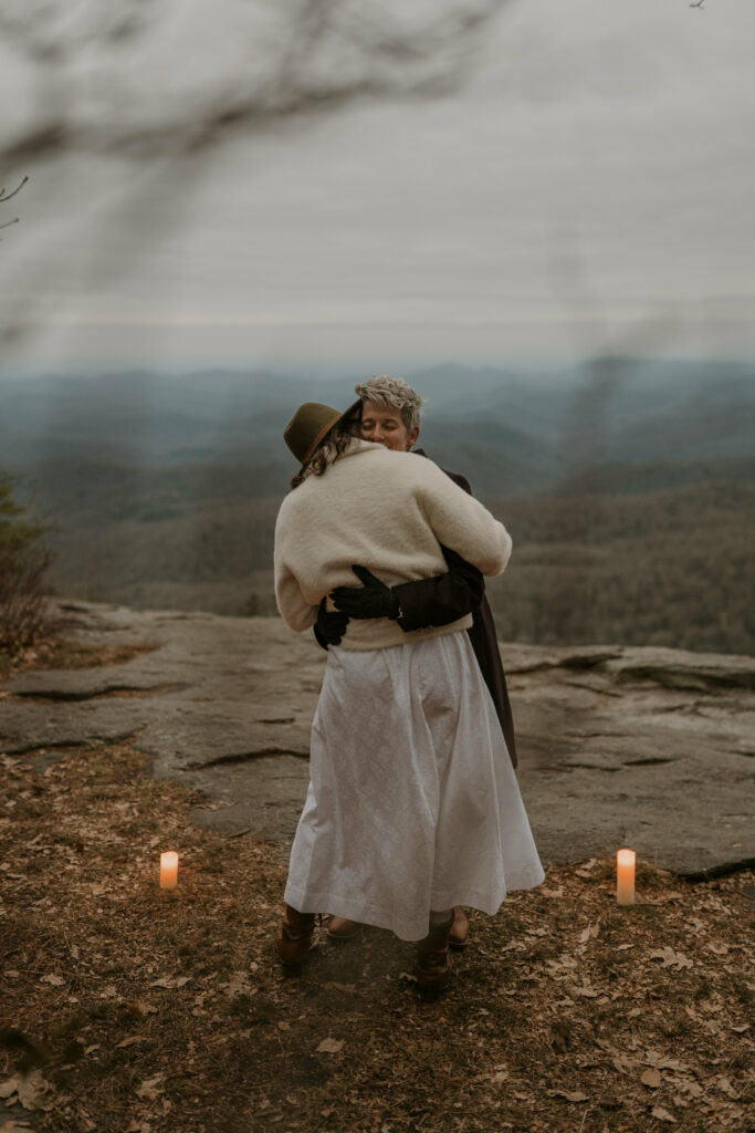 A couple hugs and dances on top of a mountain on a cloudy winter day in Western NC.