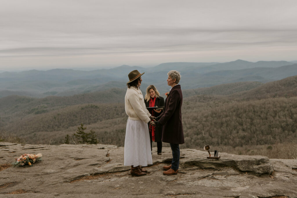 A couple is getting married on a rock with a large mountain range behind them.