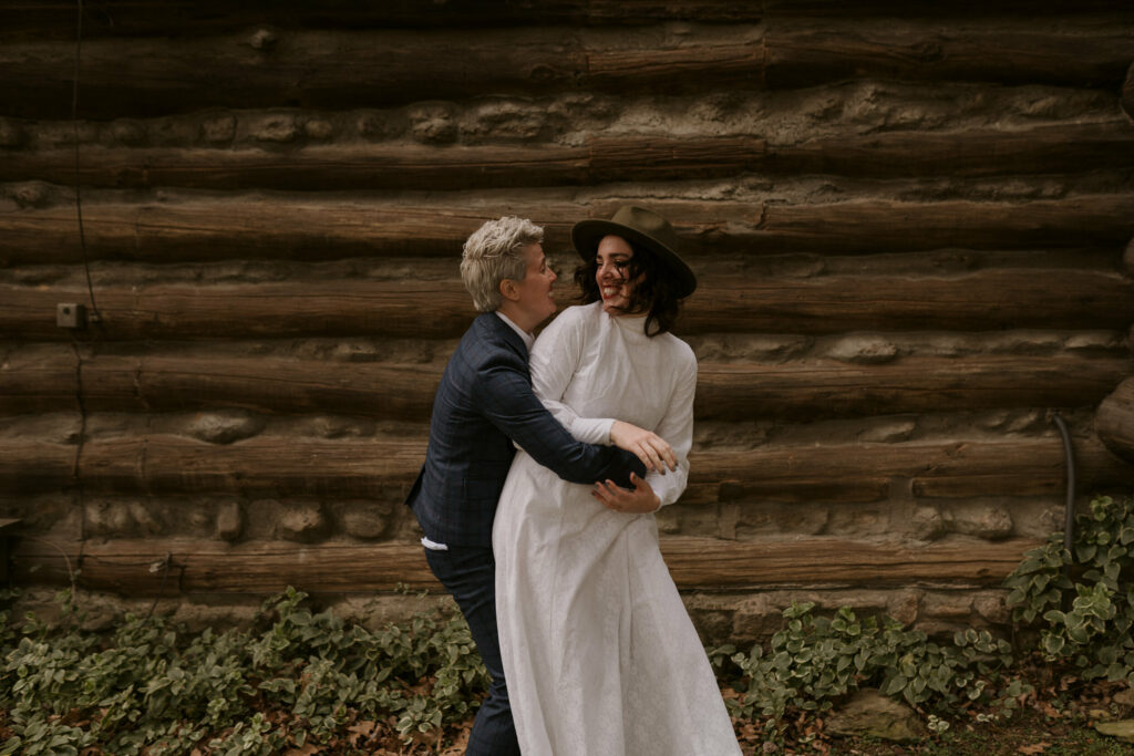 A couple snuggling outside a log cabin during wedding portraits.