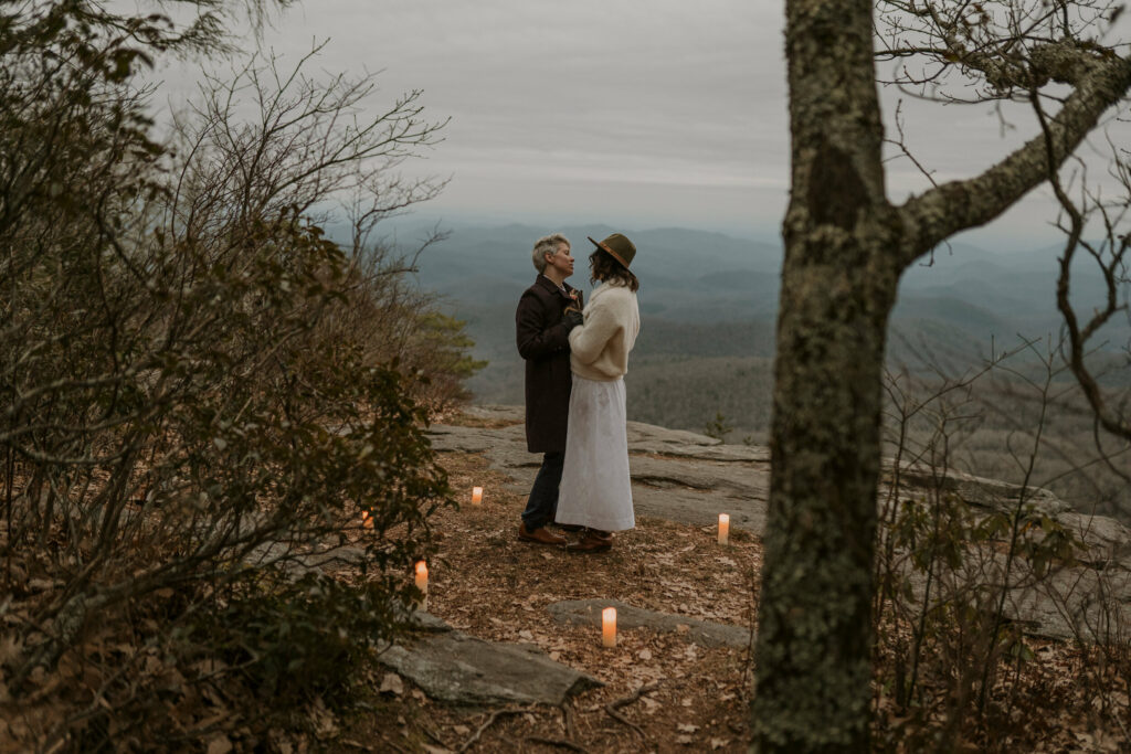 A couple dances on top of a mountain overlooking a vast vista surrounded by candles.