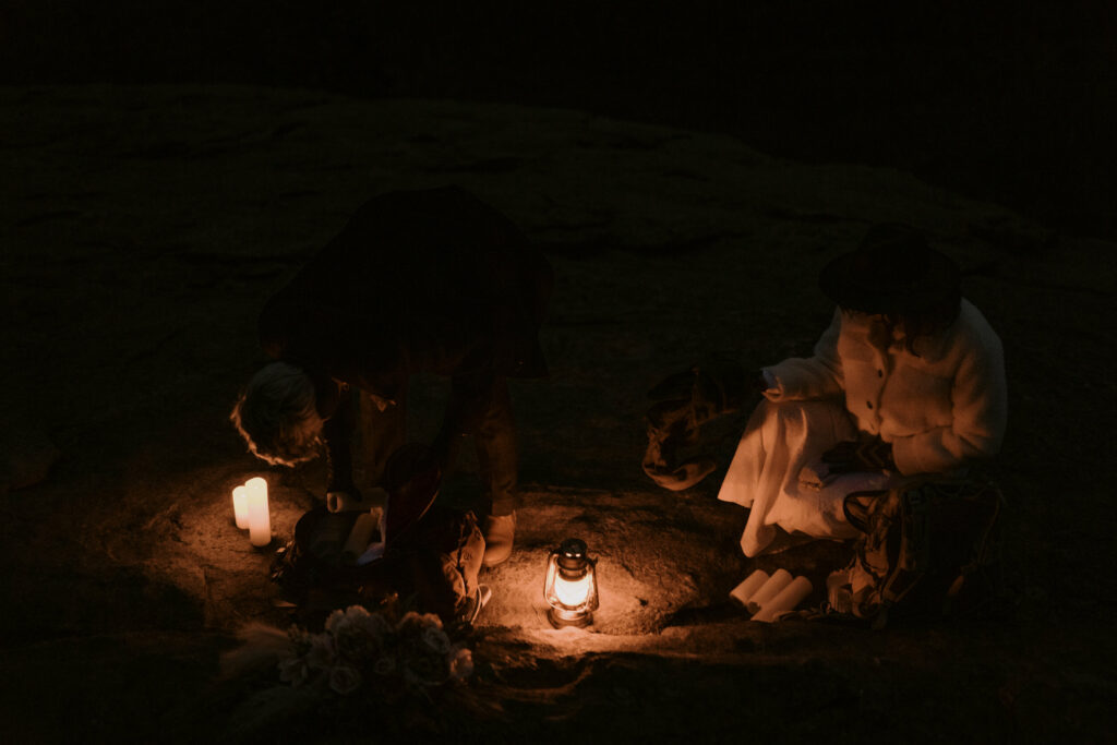 A couple sits in the dark with a lantern and some candles on top of a mountain.