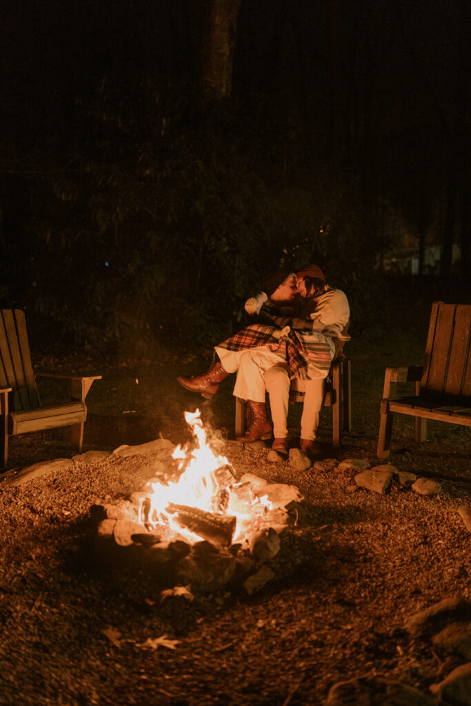 A couple relaxes by a cozy fire pit in the dark in the Blue Ridge Mountains.