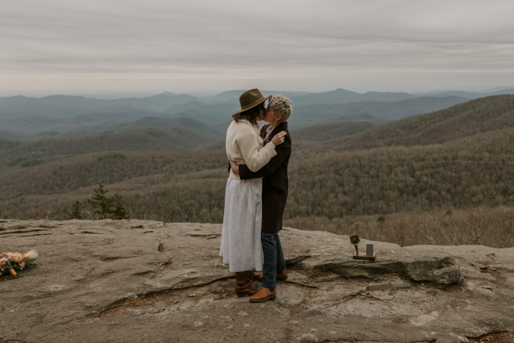 The first kiss of a married couple on top of a rock overlooking a mountain range in North Carolina.