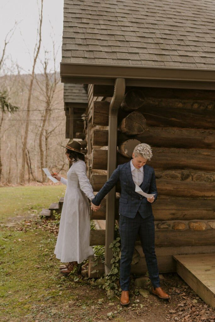 A couple holds hands around the corner of cabin before their elopement.