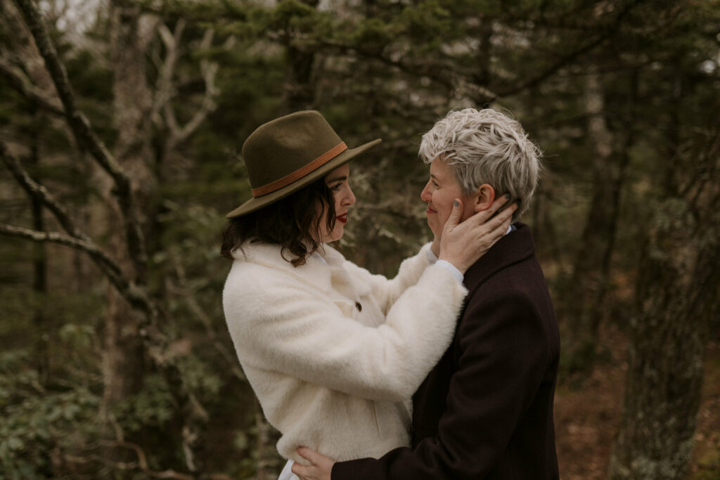 A couple holds each other in the middle of the forest in the winter.
