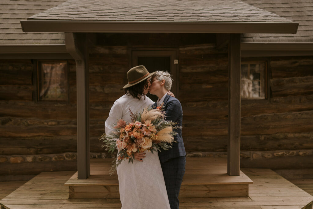 A couple kisses outside of their log cabin before their adventure winter elopement.
