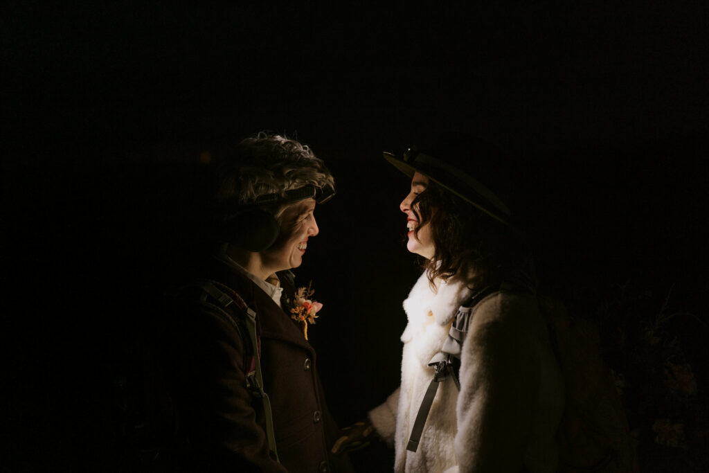 A couple laughs in the dark while wearing headlamps.
