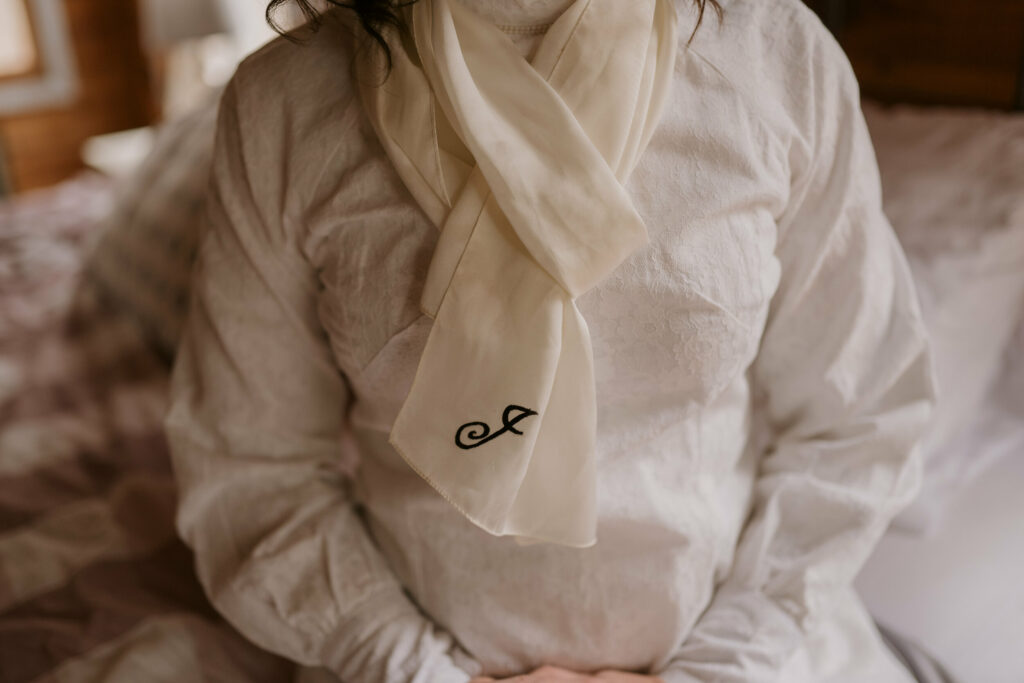 A close-up photograph of a monogrammed scarf around a person’s neck.