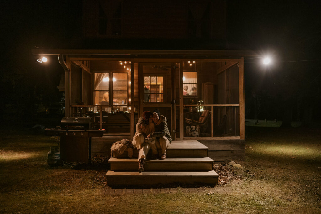A couple sits in the dark outside a lit-up cabin after their elopement.