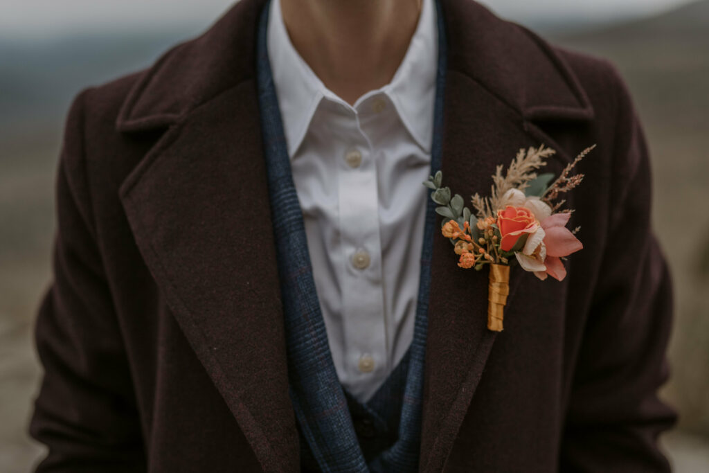A close-up of a bright orange boutonniere pinned to a dark brown suit jacket.