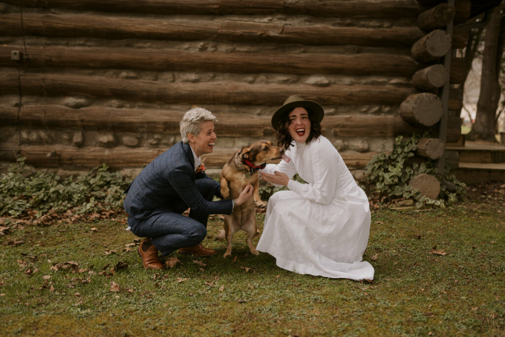 A couple laughs while taking pictures of their dog outside their cabin.
