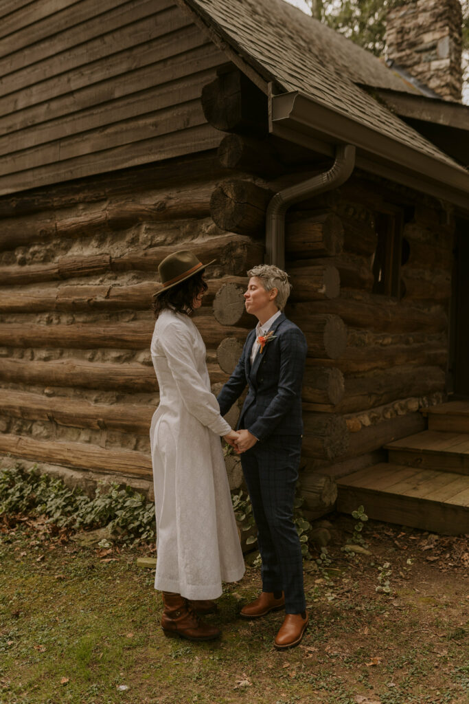 A couple stands outside of cabin in the western NC mountains holding hands.