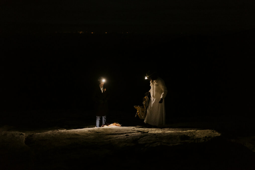A couple stands in the dark on a rock with headlamps on.