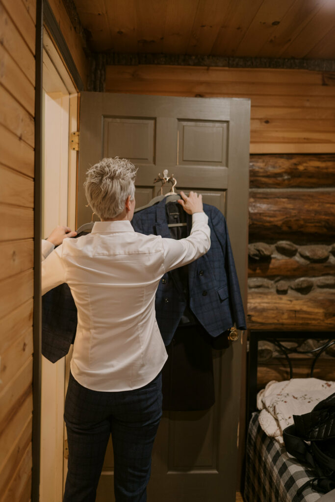 A person takes a suit off a door inside a cabin in preparation for their winter elopement.