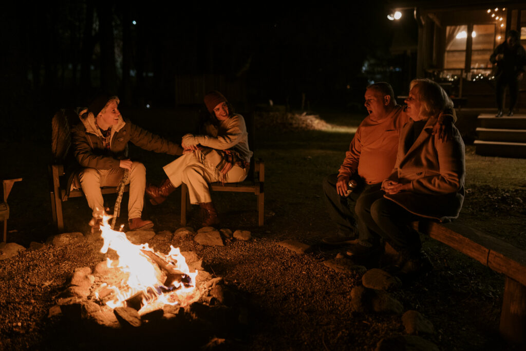 Friends and family join an elopement celebration around a campfire at night and talk.