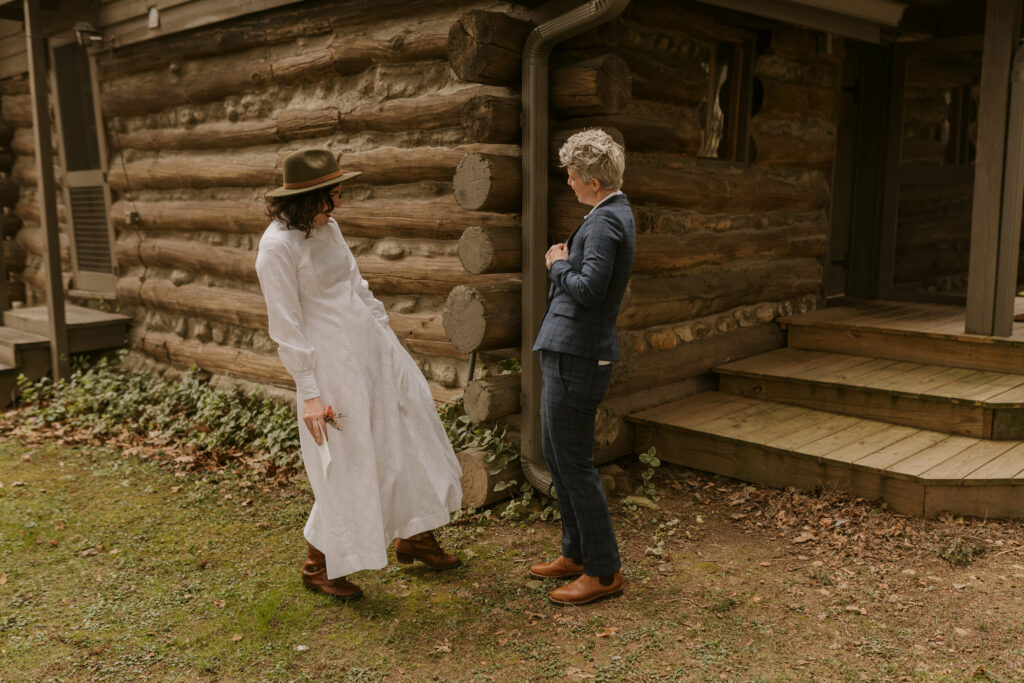 A couple shows off their wedding attire to each other outside a cabin before they get married.