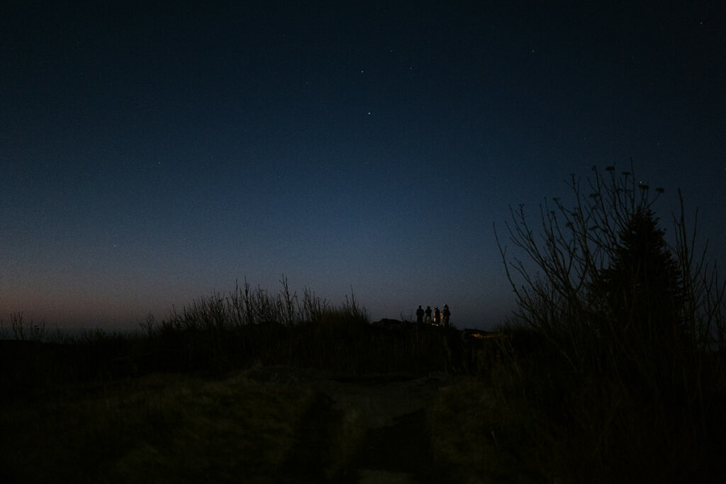 A group of people are standing together in the distance at blue hour on Black Balsam Knob in preparation for a wedding.