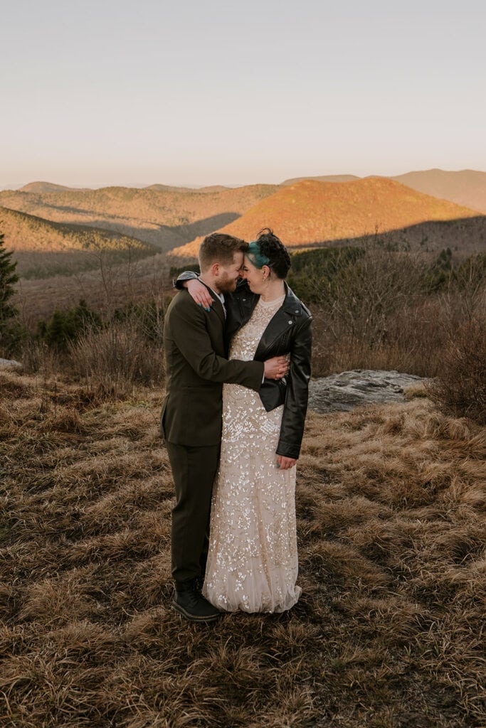 A couple is standing in their wedding clothes on a mountain at sunrise on Black Balsam Knob.