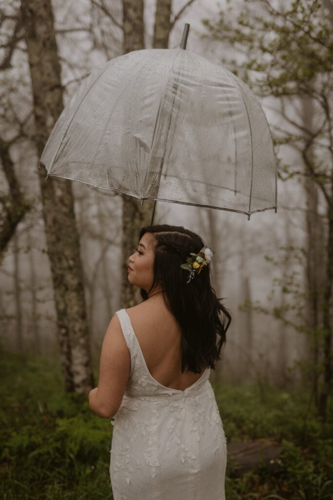 Bride in wedding dress holding an umbrella during a rainy elopement.