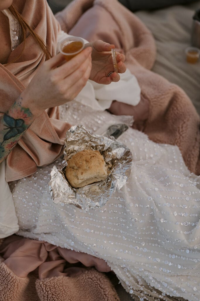 a biscuit wrapped in tinfoil is sitting in the lap of someone wearing a wedding dress and holding a little cup of jam.