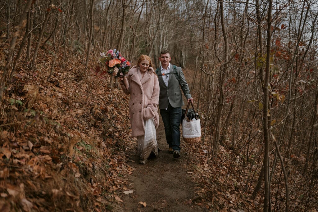 A couple walks down a winter wooden trail together after their elopement at Max patch