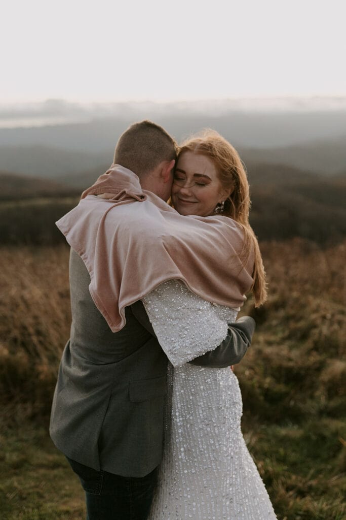 A couple is snuggled up in front of a mountain view in their elopement clothes.