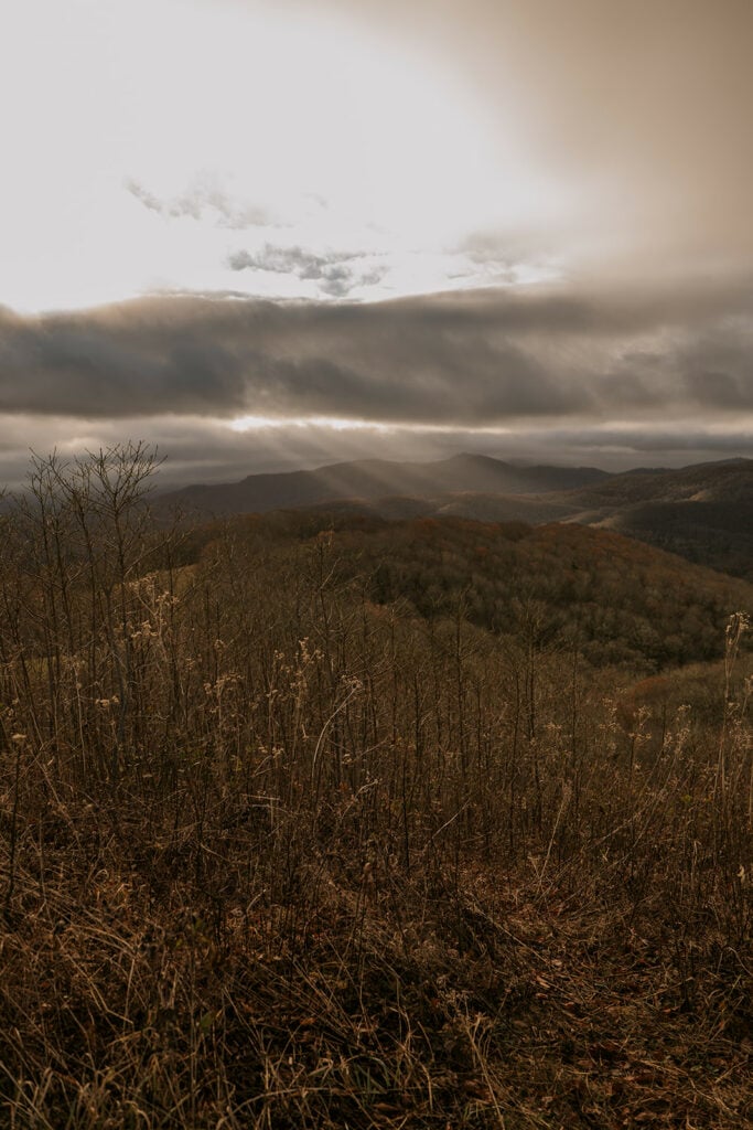 A landscape view of fall mountains with light beaming through the clouds.