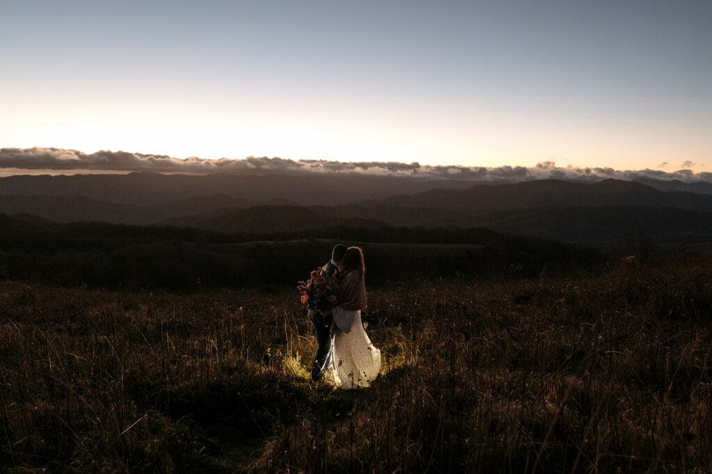 A couple is hugging and facing the view of the mountains right before sunrise on Max Patch for their elopement.