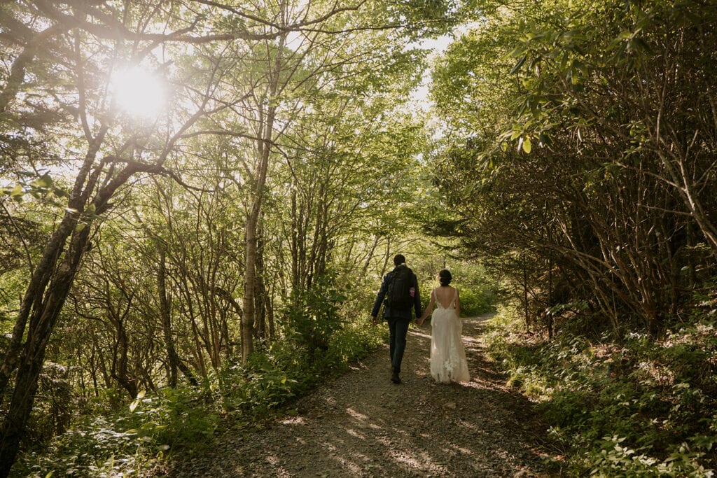 A couple is hiking through a lush, green forest holding hands with their wedding clothes on for their Jewish elopement.