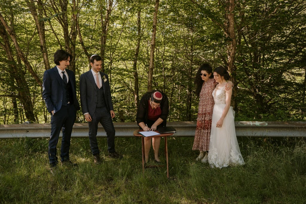 A rabbi is signing paperwork while a bride and groom stand by with their siblings during their Jewish elopement.
