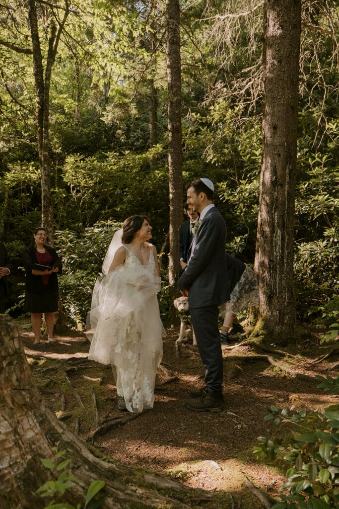 A bride walks around her groom during the beginning of their Jewish elopement ceremony in the woods.