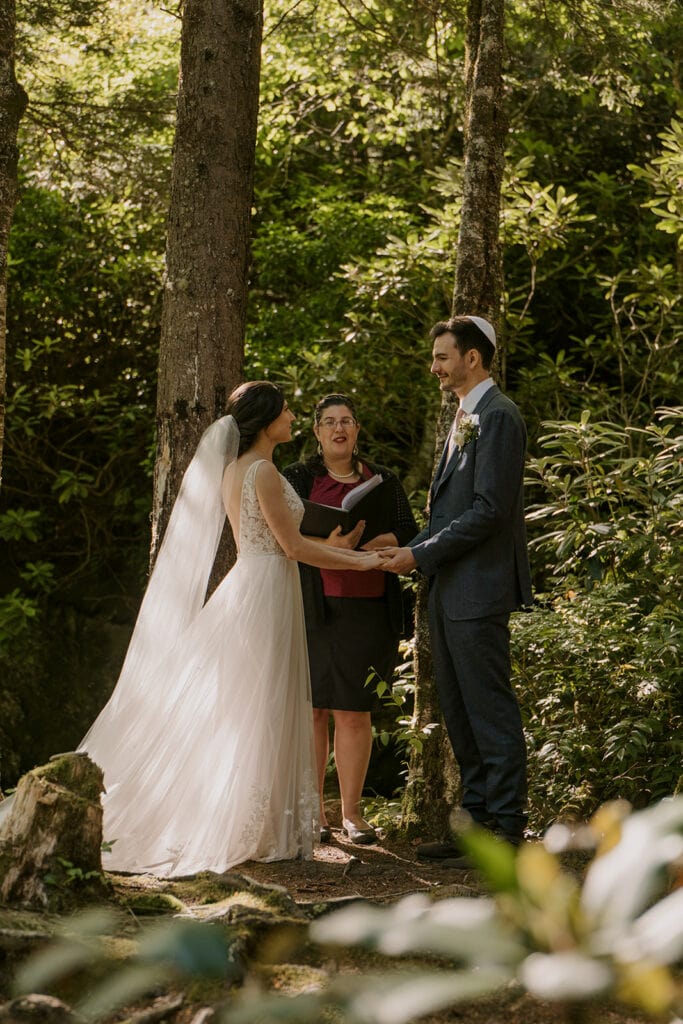A couple stands holding hands during a Jewish elopement in the forest.