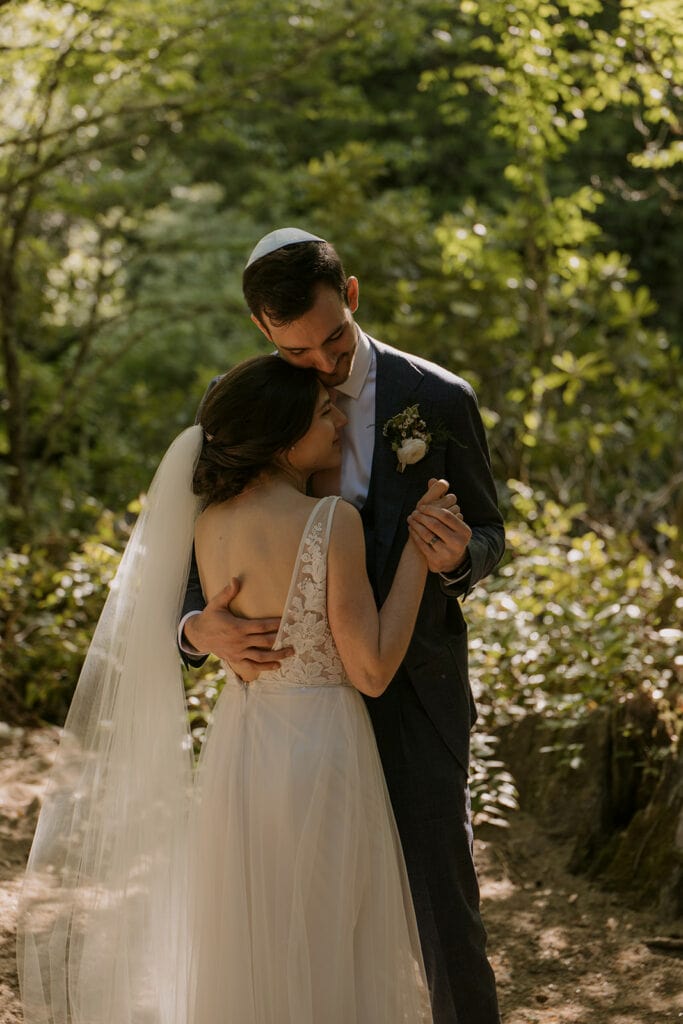 A couple is dancing and holding each other close in a lush, green forest during their Jewish elopement.